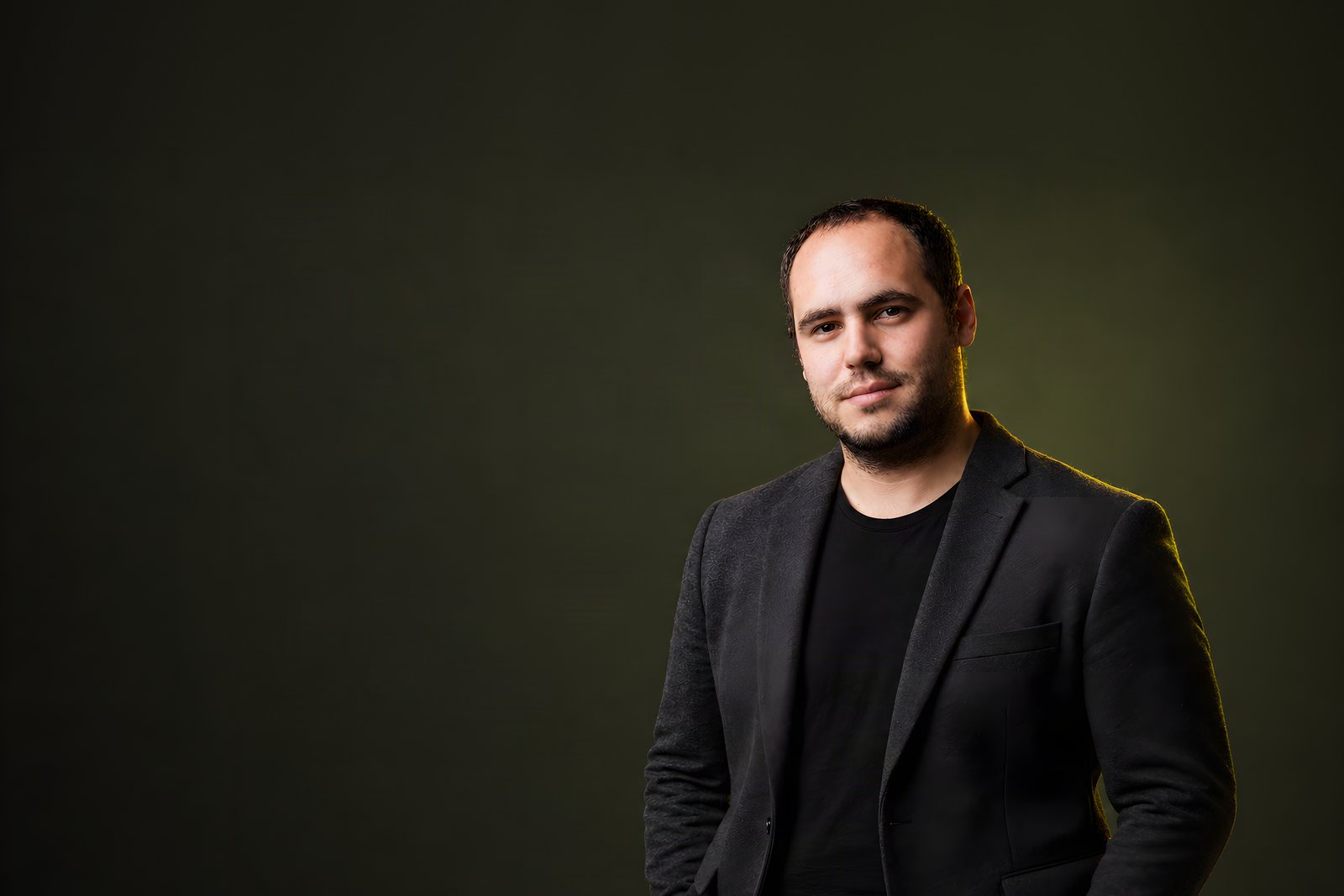 Rom Ribak in a charcoal blazer, on an olive background